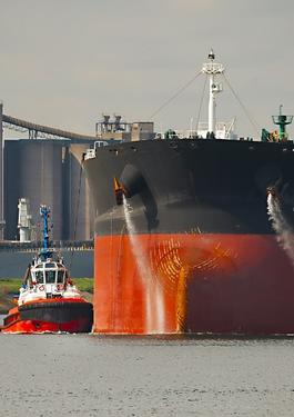 Large crude oil tanker ship pumping out ballast water when coming into port in Rotterdam, tug boat pushing the side